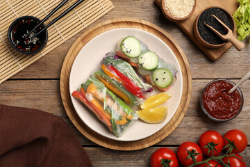 Delicious rolls wrapped in rice paper on wooden table, flat lay
