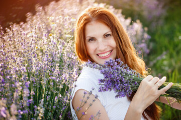 Beautiful smiling woman in lavender field. Beauty portrait of girl with lavender bouquet flowers. Close up face with freckles and red long hair