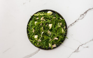 Delicious light salad with arugula, mozzarella and chicken breast in a plate on a white marble background, top view