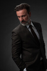 Portrait of a stylish elegant senior businessman with a beard and casual business clothes in photo studio isolated on dark background gesturing with hands