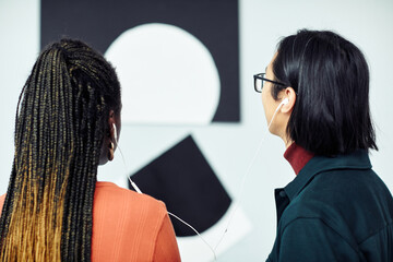 Back view of ethnically diverse young couple looking at picture and listening to audio tour at exhibition in contemporary art gallery
