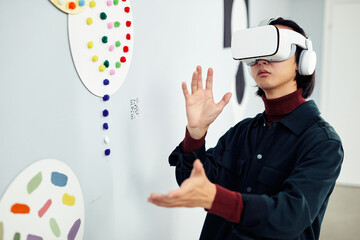 Portrait of young Asian man wearing headset visiting modern exhibition looking at artworks using...