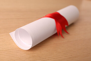 Graduation diploma tied with red ribbon on wooden table, closeup