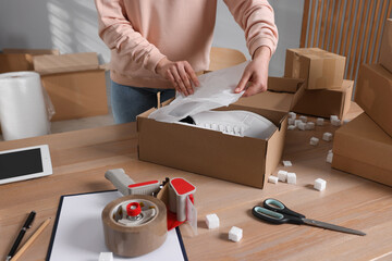 Seller packing shoes into cardboard box at table in office, closeup. Online store