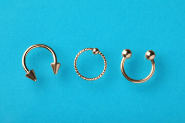 Different stylish rings for piercing on light blue background, flat lay