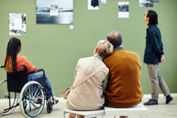 Back view of unrecognizable mature man and woman in love sitting together in modern art gallery...