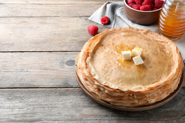 Stack of delicious crepes served with butter, honey and raspberries on wooden table. Space for text