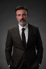 Portrait of a stylish elegant senior businessman with a beard and casual business clothes in photo studio isolated on dark background gesturing with hands