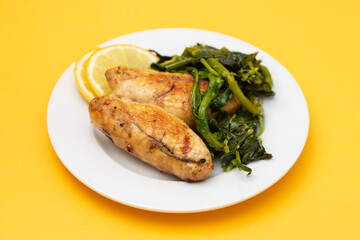 Grilled caviar cod fish with greens and fresh lemon on white small plate.