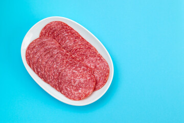 fresh cut salami on small white plate on blue