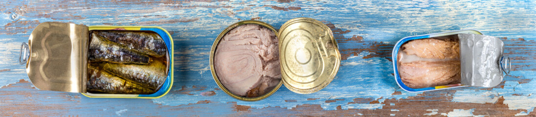 Panoramic image, Various canned fish and seafood in a metal cans. Wooden blue background. Top view