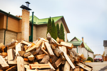 A pile of split firewood for heating the house, unloaded in the yard, against the backdrop of the house, natural heating sources.
