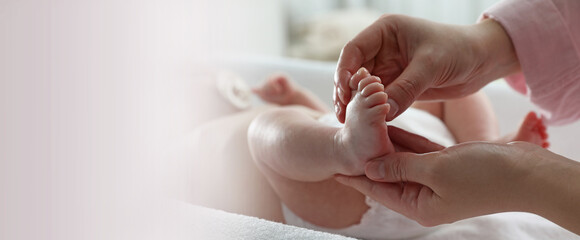 Mother massaging her cute baby with oil on changing table, closeup. Banner design with space for text