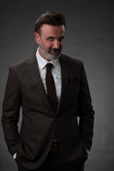 Portrait of a stylish elegant senior businessman with a beard and casual business clothes in photo studio isolated on dark background gesturing with hands