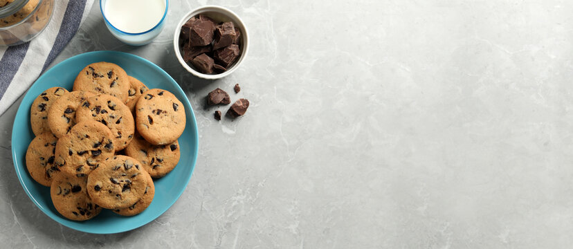 Delicious chocolate chip cookies and glass of milk on grey marble table, flat lay with space for text. Banner design