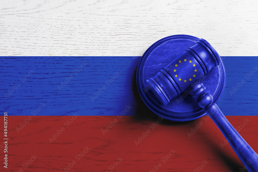 Wall mural Judge's gavel on wooden background in colors of Europenean Union and Russian flags, top view. Concept of sanctions against Russia