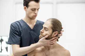 Fototapeta premium Physical therapist does manual therapy to a young athletic guy at medical office. Concept of manual therapy and osteopathy