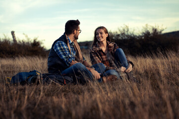 Naklejka na ściany i meble Couple sitting on grass during sunset resting after hiking.