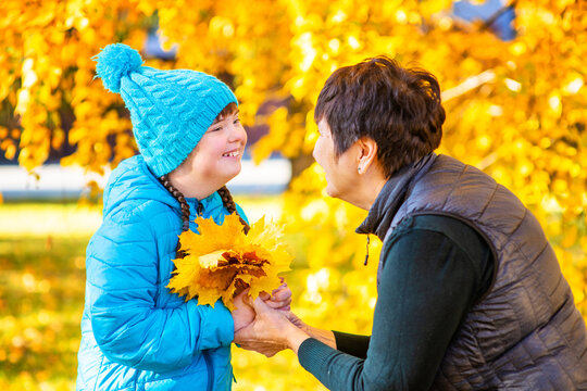 A girl with her mother outdoors in an autumn park collecting a bouquet of fallen leaves