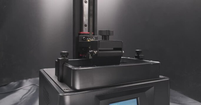 Working consumer resin MSLA 3D Printer during 3d printing.  Build plate moving up and down in the resin vat with linear rail in the back.
