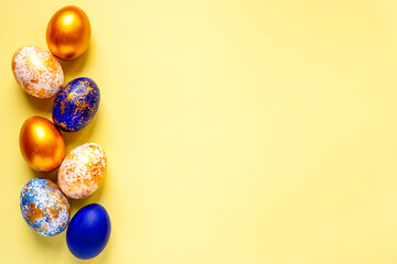 colored golden, blue, light blue Easter eggs on a yellow background for Easter