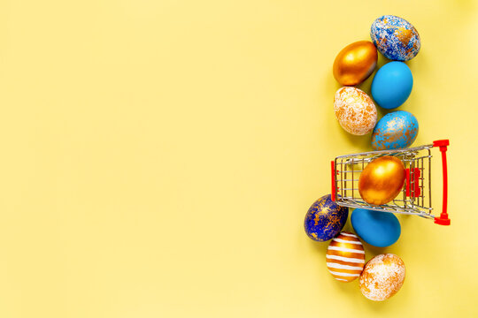 colored golden, blue, light blue Easter eggs on a yellow background for Easter with a grocery cart