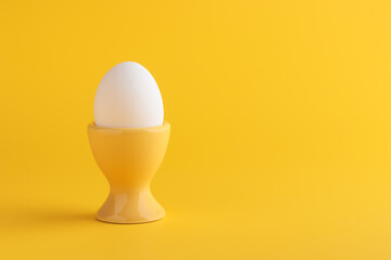 White fresh egg in the yellow egg stand, cup for breakfast on solid yellow background, vertical...