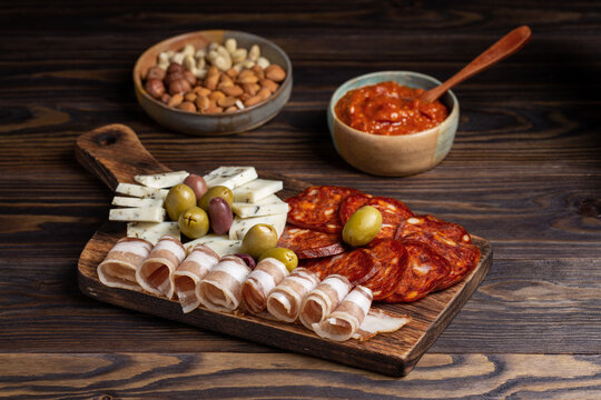 Charcuterie and cheese plate on wooden background. Serbian meze - kulen sausage, balkan bacon, goat cheese, olives and ajvar sauce.