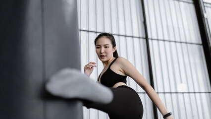 Fototapeta na wymiar exercise concept The boxing woman being concentrated on knocking the boxing weighty bag by one of her legs