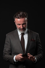 Portrait of adult businessman wearing trendy suit and sitting in modern studio on stylish chair against the black background
