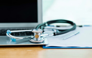 Stethoscope with clipboard and laptop on docotr desk