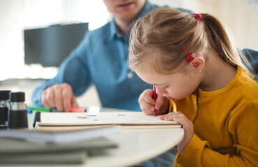 Father with his little daughter with Down syndrome learning at home.