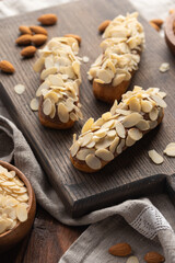 Eclairs with almond petals on a wooden board