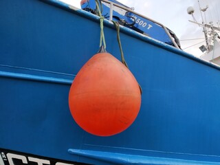 Red bollard on the blue hull of a fishing boat.
