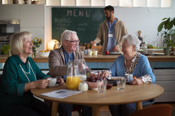 Group of cheerful seniors enjoying breakfast in nursing home care center.