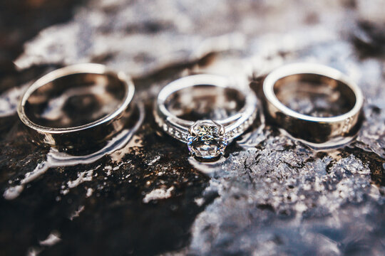 Three wedding rings of gold, platinum, silver and precious stones. Close-up portrait on the surface of a wet stone. Engagement ring.