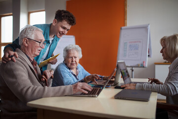 Senior group in retirement home with young instructor learning together in computer class