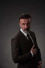 Portrait of a stylish elegant senior businessman with a beard and casual business clothes in photo studio isolated on dark background gesturing with hands