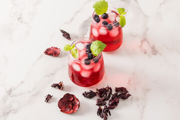 two glass glasses with cold hibiscus tea, blueberries, lime slices and ice cubes on a marble table. high content of vitamins, antioxidants. © Marina