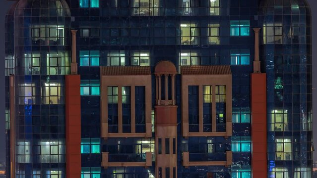 Night aerial view of apartment building glass window facade with illuminated lighted workspace rooms timelapse.