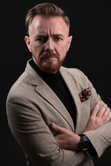 Fototapeta premium Portrait of a stylish elegant senior businessman with a beard and casual business clothes in photo studio isolated on dark background gesturing with hands