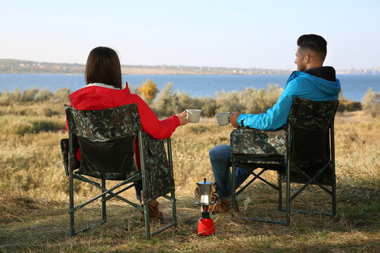 Couple Resting In Camping Chairs And Enjoying Hot Drink Outdoors, Back View