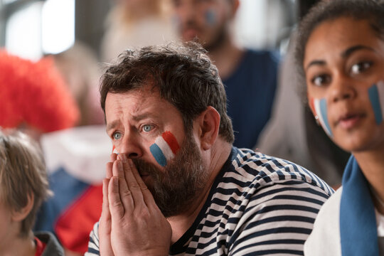 Worried football fans supproting French national team in live soccer match at stadium.