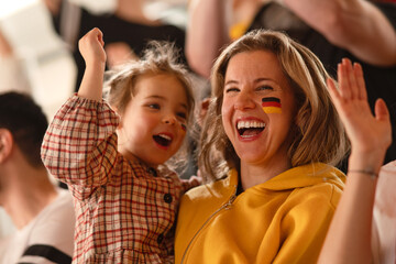 Fototapeta premium Excited football fans, mother with little daughter, supproting German national team in live soccer match at stadium.