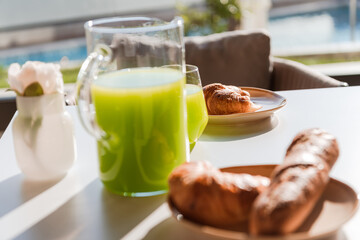 Healthy breakfast served on wooden table in space with window and natural light with yogurt and green smoothie in glasses and glass jar, chopped bread on black plate .