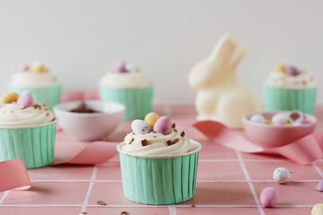 Easter egg cupcakes in mint green cases set against a pale pink background. Pastel spring colour theme. Chocolate easter egg celebration food.