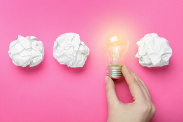Woman holding lightbulb among paper balls on pink background, top view. Idea concept