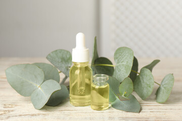 Bottles of eucalyptus essential oil and plant branches on white wooden table
