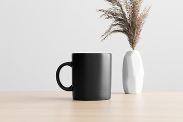 Black mug mockup with a dry flower decoration on the wooden table.