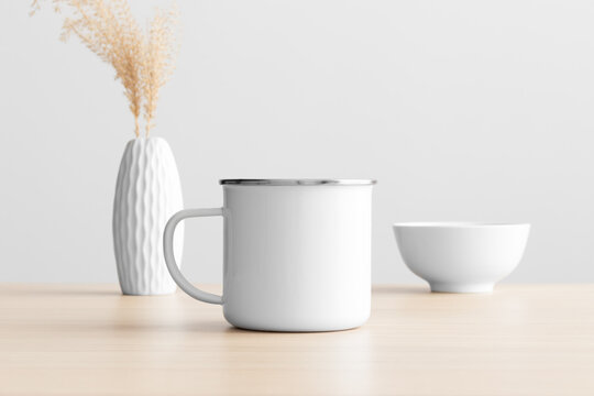 Enamel mug mockup with a dry flower decoration on the wooden table.